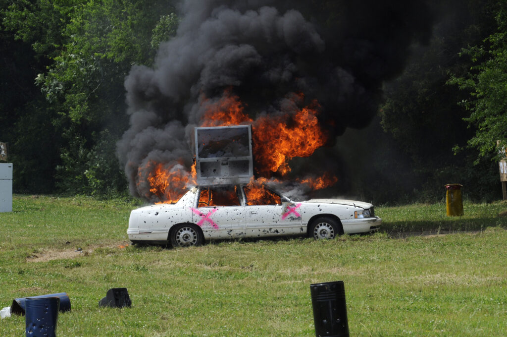 White target car on fire with heavy smoke during a live-fire demonstration at Terra Bellum
