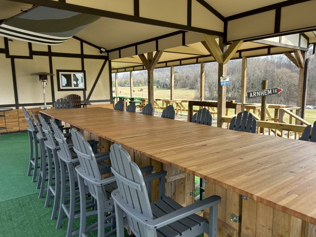 Large outdoor wooden dining and meeting table with seating under a covered pavilion at Terra Bellum