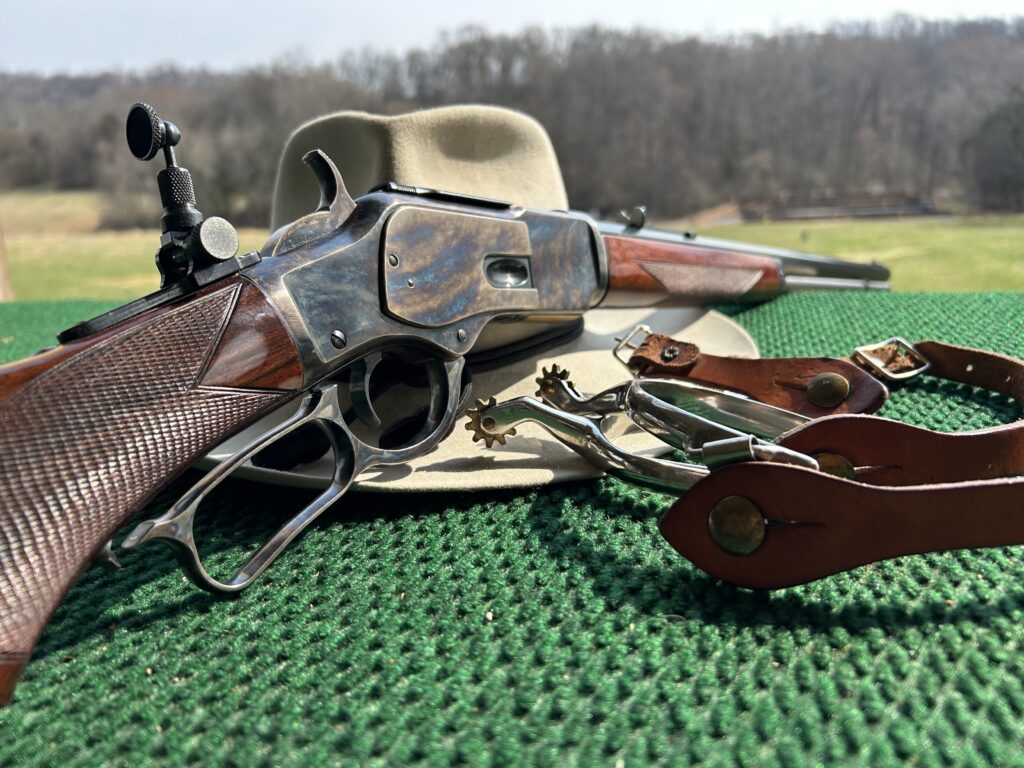 Classic lever-action rifle, cowboy hat, and leather spurs on a shooting bench at Terra Bellum