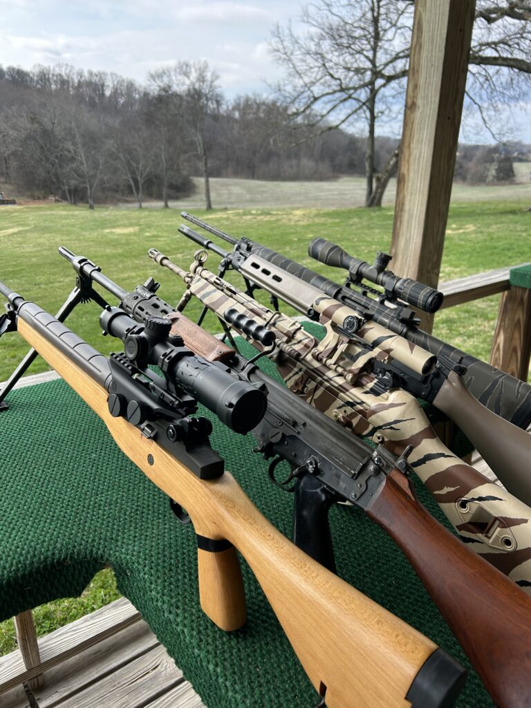 Scoped battle rifles displayed on a covered shooting range bench at Terra Bellum