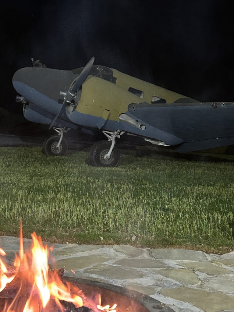 Nighttime fire pit with a vintage military twin-engine aircraft display at Terra Bellum