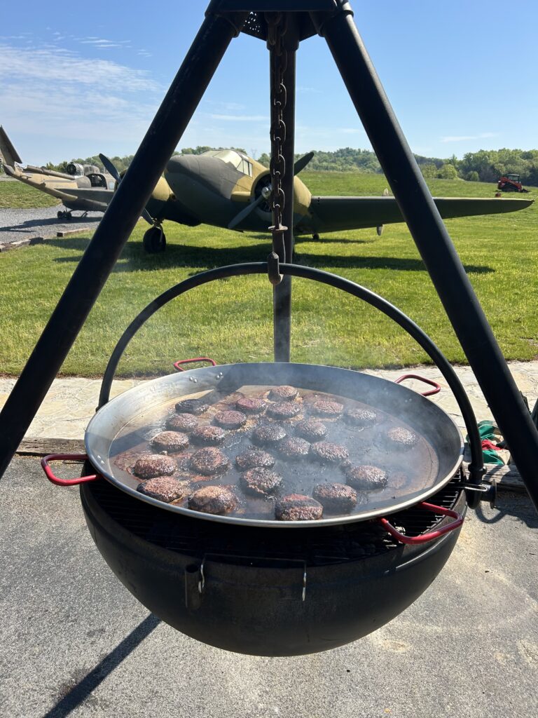 Outdoor event catering featuring burgers cooked on a tripod skillet at Terra Bellum