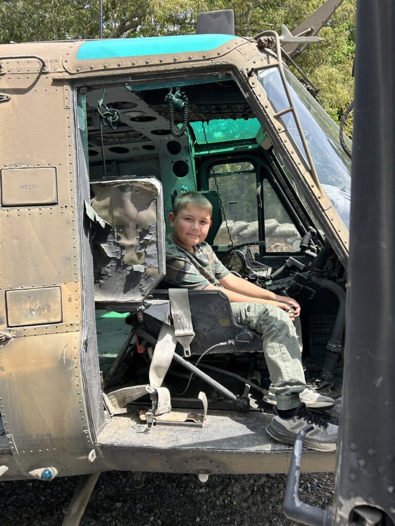Young boy sitting inside the cockpit of a historic UH-1 Huey military helicopter display at Terra Bellum